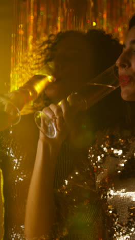 Vertikales-Video-Von-Zwei-Frauen,-Die-In-Einem-Nachtclub-Oder-Einer-Bar-Tanzen,-Jubeln-Und-Bei-Funkelnden-Lichtern-Alkohol-Trinken